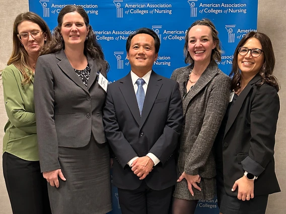 Five people standing in front of a American Association of Colleges of Nursing banner